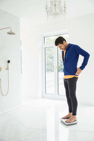 Mature man weighing himself on bathroom scales