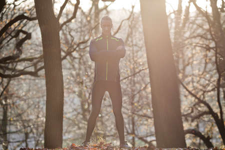 Full length front view of mid adult man standing in forest arms folded looking at camera smiling
