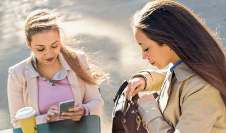 Young adult female twins reading smartphone texts at sidewalk cafeの写真素材