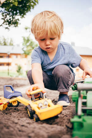 Boy crouching in mud looking down playing with toy trucksの写真素材