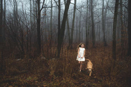 Girl wearing white dress walking her dog in forestの写真素材