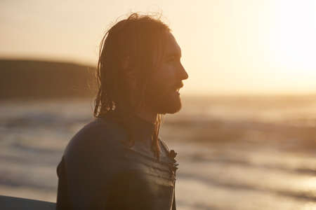 Young male surfer looking out from beach, Devon, England, UKの写真素材
