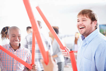 Colleagues in team building task, holding red tubes smiling