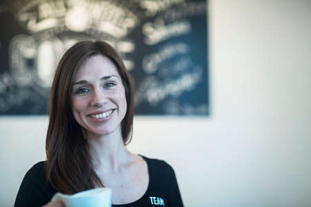 Portrait of young female waitress holding coffee in cafe