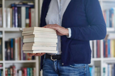 Cropped shot of woman carrying stack of books from bookshelvesの写真素材
