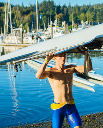 Teenage boy holding sculling boat above headの写真素材