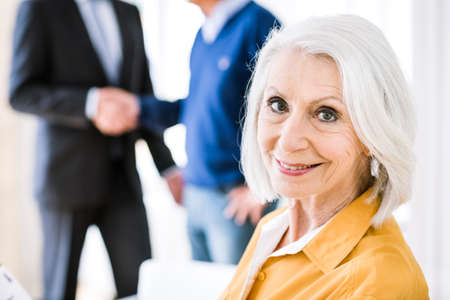 Senior woman in business meeting looking over shoulder at camera smiling
