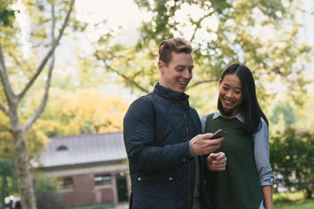 Mid adult couple in park reading smartphone texts
