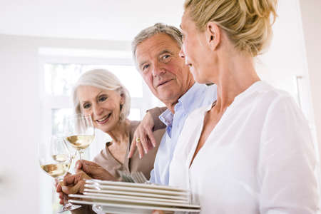Senior couple and mature woman raising a glass of wine to each other in kitchenの写真素材
