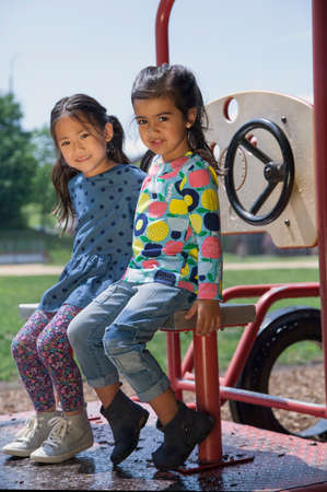 Portrait of two girls sitting on playground climbing frameの写真素材