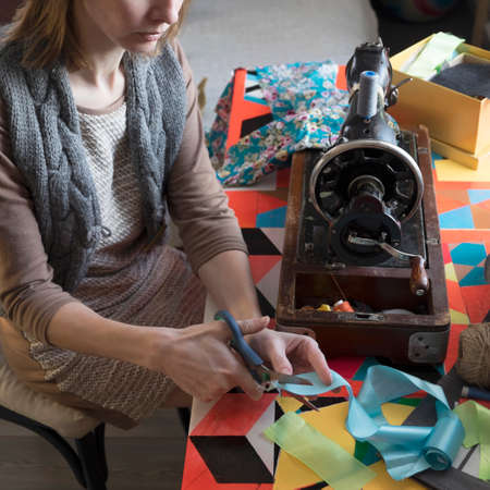 Woman with vintage sewing machine cutting ribbon at tableの写真素材