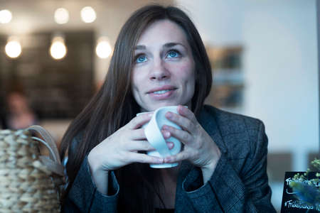 Young woman looking up whilst drinking coffee in cafe