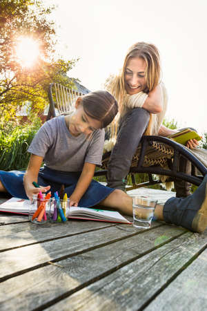 Daughter sitting on wooden decking drawing with mother