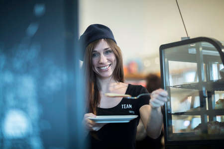 Portrait of young female waitress holding plate and cake slice in cafeの写真素材