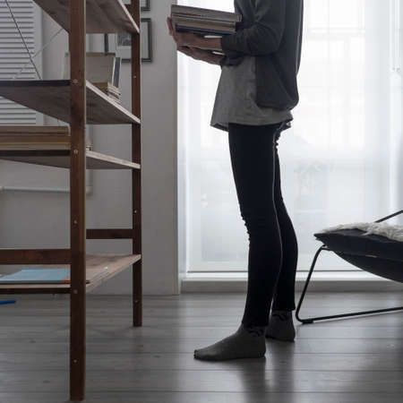 Cropped view of woman arranging books on living room bookshelfの写真素材