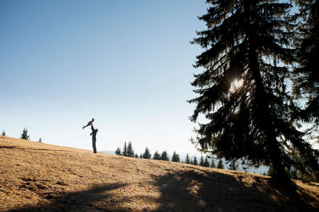 Silhouette of man holding up toddler daughter on hill, Tegernsee, Bavaria, Germanyの写真素材