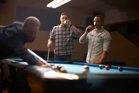 Man playing pool, friends drinking beer in backgroundの写真素材