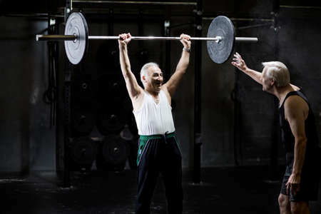 Senior men training with barbell in dark gymの写真素材