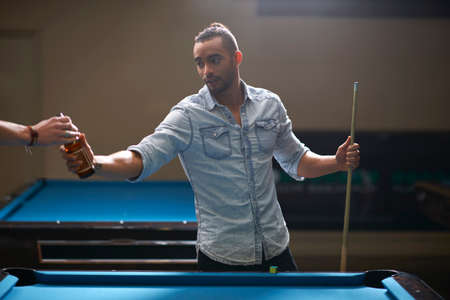 Man taking beer from friend at pool tableの写真素材