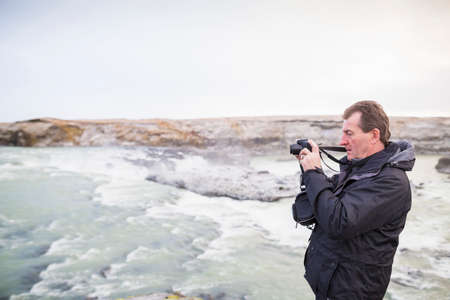 Senior man photographing waterfall, Icelandの写真素材
