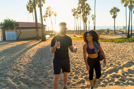 Couple wearing sports clothing, walking along beach, talkingの写真素材