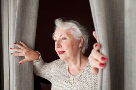 Senior woman, opening curtainsの写真素材