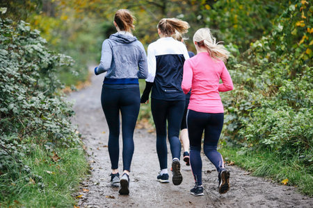 Rear view of teenage girl and women running in parkの写真素材