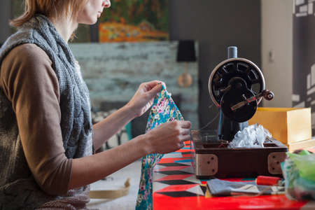 Woman with vintage sewing machine inspecting fabric at tableの写真素材