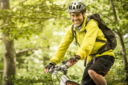 Happy mature male mountain biker cycling in forestの写真素材