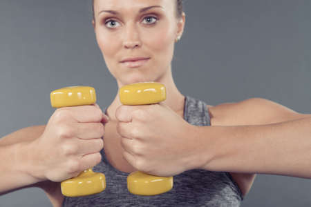 Young woman working out with dumbbells, grey background
