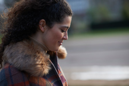 Side view of curly haired woman wearing tartan fur trim coat looking down smiling