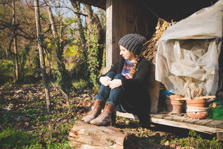 Young woman sitting in storage shed wearing knit hat looking awayの写真素材
