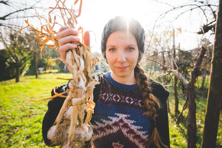 Young woman in garden holding freshly picked garlic bulbs looking at camera smilingの写真素材