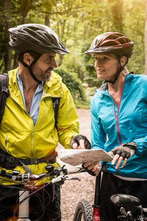 Mature mountain biking couple checking map in forestの写真素材