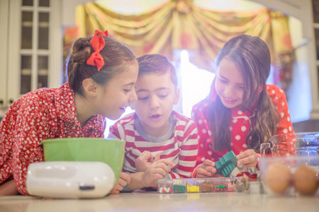 Children wearing pyjamas at kitchen counter discussing cake decorationsの写真素材