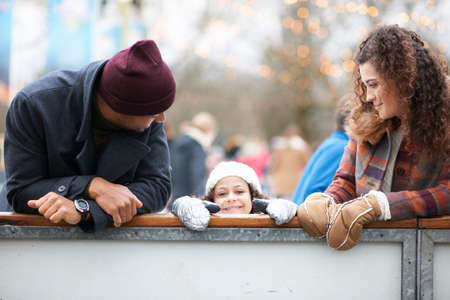Girl with parents peeking over barrier, looking at camera smilingの写真素材