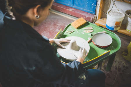 Over shoulder view of young woman sitting using pottery wheelの写真素材