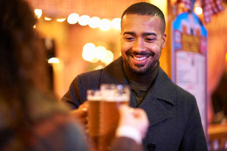 Couple on night out, holding beer glasses making a toast smiling