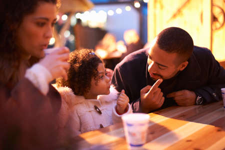 Girl at amusement park sitting at table with father talking