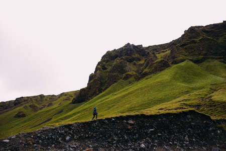 Mid adult woman hiking below lush green mountain range, Iceland