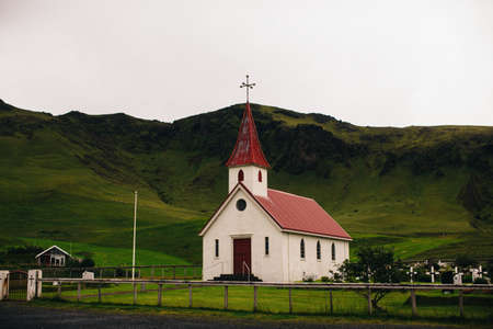 Village church below lush green mountain range, Icelandの写真素材