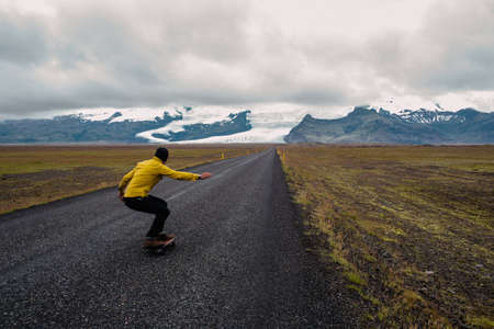 Rear view of mid adult man skateboarding to snow covered mountain range, Icelandの写真素材