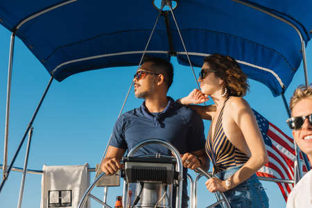 Couple behind wheel of sailboat, enjoying view with friendの写真素材