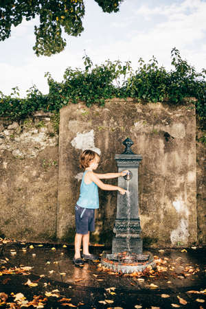 Side view of boy using outdoor drinking fountain, Luino, Lombardy, Italyの写真素材