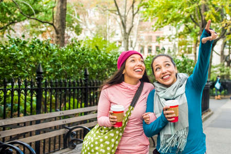 Twins walking with coffee and pointing up in park