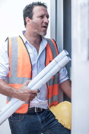 Construction foreman with blueprints at doorway of portable cabin on construction site