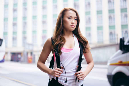 Young woman carrying backpack waiting on city streetの写真素材