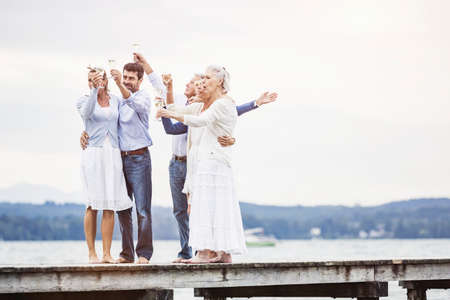 Group of friends standing on pier, holding wine glasses, making a toastの写真素材