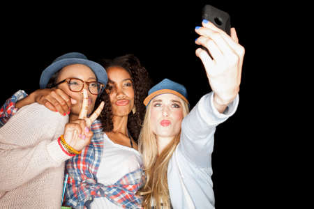 Young women huddled together making peace sign, puckering lips, using smartphone to take selfie