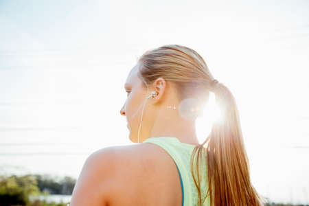 Low angle rear view of woman with ponytail wearing earbuds looking awayの写真素材